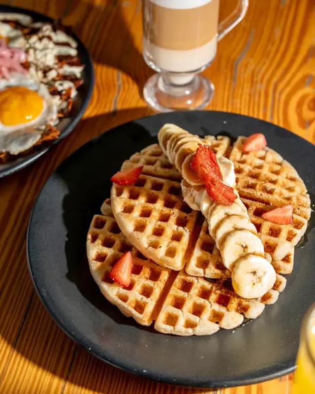 Waffle con fresa y plátano, huevo y café con leche en vaso alto.
