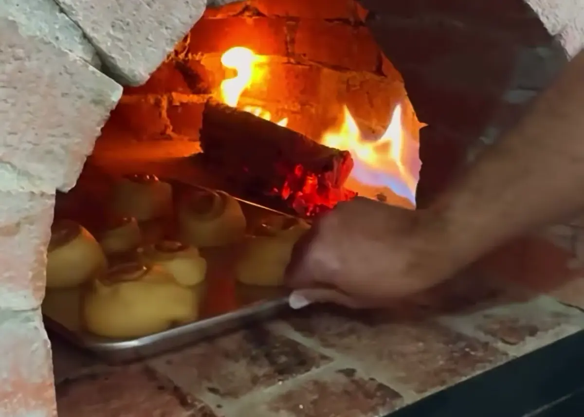 El horno de bóveda de ladrillo encendido, con la pala metiendo una charola de pan.