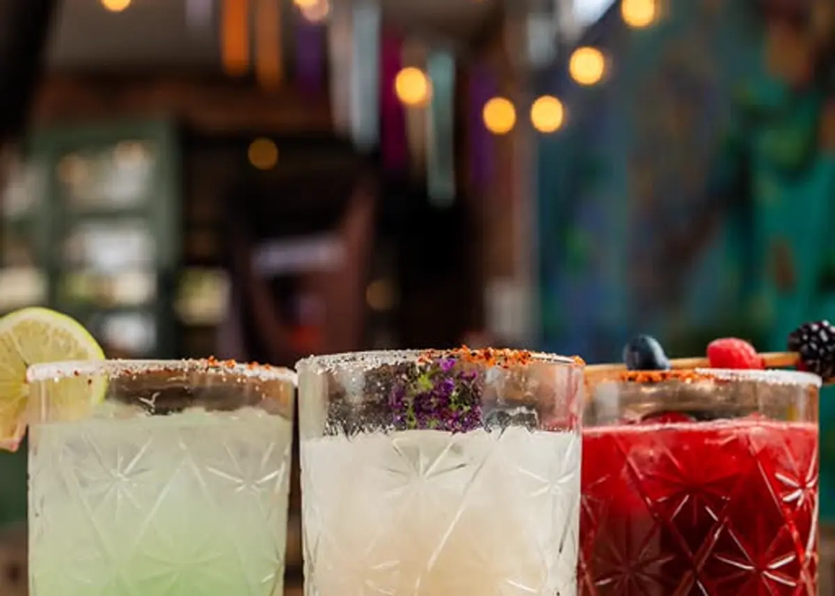Tres mezcalitas de temporada en vaso bajo, con las luces colgantes de la terraza detrás.